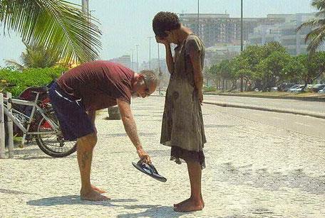 Brezilya Rio'da, ayakkabs olmayan evsiz bir yerliye ayandaki terlikleri veren turist.