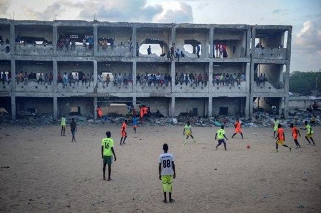 1991'de terk edilmi bir okulun kalntlar, Somali'nin Mogadiu kentinde tozlu bir sahada  derme atma odacklar iinde ma izleyen futbolseverler.