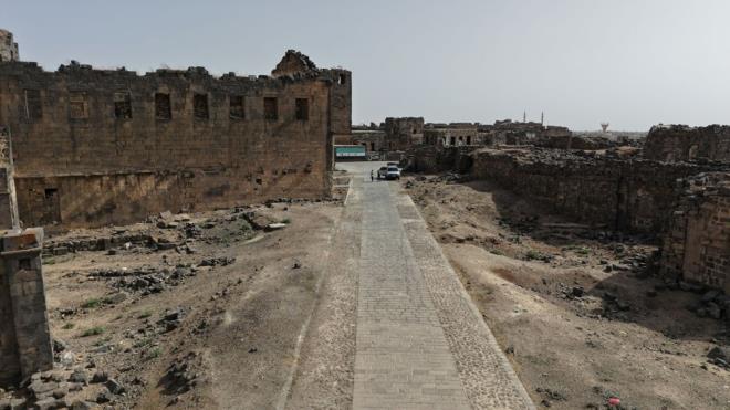 AA ekibi, Rahip Bahira'n�n ad�n� ta��yan manast�r�n g�n�m�zdeki son halini g�r�nt�ledi.<br><br>Yakla��k 1500 y�l �nce in�a edildi�i de�erlendirilen manast�rdan, g�n�m�ze yaln�zca baz� kal�nt�lar ula�abildi. Erken Hristiyanl�k d�nemine ait oldu�u d���n�len yap�n�n ta� duvar par�alar�, s�tun temelleri ve apsis b�l�m�n�n izleri halen ayakta duruyor.<br><br>Kentte tur rehberli�i yapan b�lge sakinlerinden Ahmed el-Mikdad, "Buras� antik bir kent. Buras� Hz. Muhammed'in �ocukken Rahip Bahira ile kar��la�t��� b�lge olarak bilinmektedir. Bahira burada Peygamber Efendimiz ile tan��t�. Busra �ehrinde (antik kent ve �evresi) sava� �ncesi yakla��k 40 bin ki�i, Antik kentin merkezinde ise sadece 5 bin ki�i ya��yordu. �nsanlar burada ya��yordu ve �nemli turistik bir yerdi. Esed rejimi ve �ran destekli milislerin sald�r�lar� sonucu b�lge halk�n�n y�zde 99'u g�� etti. Manast�r sald�r�lardan zarar g�rd�." dedi.