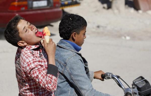 Rakka'da bir ocuk arkada ile birlikte bindii motosiklette bir yandan yolculuk ederken, bir yandan da dondurmasnn keyfini karyor.     <p><b<Suriye</b></p>
