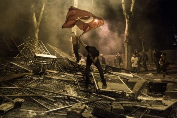 stanbul, 1 Temmuz 2013 - Fotoraf: Daniel Etter Protestolarn bykl karsnda ok olmutum. Taksim Meydan'nn yaknlarnda yaadm iin ufak protestolara olduka alkndm, bu yzden Gezi Park protestolar ilk balarda bana sradan gzkmt. Hatta bu yzden zel bir haber iin Ukrayna'ya gittim. Ukrayna'ya varr varmaz, protestolarn Gezi Park zelinden kp babakan Recep Tayyip Erdoan' protesto gsterilerine dntn anladm ve hemen geri dndm. Ertesi gece, Dolmabahe'deki Babakanlk Ofisi nndeki protestolar fotorafladm. Protestocular ofise doru hareket etmeye alyor, polisler de TOMA ve ar derecede gaz ile karlk veriyordu. Protestocular polisin iini zorlatrmak iin her yere barikat kuruyordu. Barikatlarn birinin stnde bu genci grdm. Bir yandan Trk bayra sallyor, dier yandan gazn etkisi ile iki bklm olmu vaziyetteydi. Gaz maskesi takmama ramen zar zor nefes alyordum ve bu kareyi fotorafladm. Fotoraf dakikalar ierisinde viral oldu. Facebook'uma postladm ve Trk arkadalarm facbook ve twitter'dan paylamaya baladlar. lk birka saat ierisinde 10.000 kii fotoraf paylamt bile. Daha sonra bu kare t-shirtlere bask, posterlere konu oldu. Hatta zmir'de ant bile yapld.