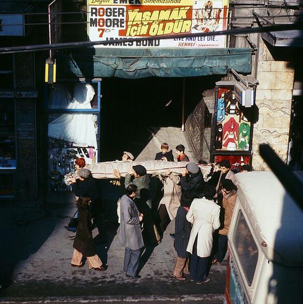 Emek sinemas var!.. Roger Moore oynuyor, James Bond var!... Zeki Alasya, Halit Akatepe, Metin Akpnar, Kemal Sunal, Mnir zkul Tark Akan var!.. Hal iinde kimse yok ama gya Emel Sayn var!.. Beyolu'nda gneli bir gn var ve irket ofisinden bir kamera ile gya gizli ekim var!.. Tannmamak iin oyuncularda apka bere kasket var ama en fazla iki dakkan var!.. Tek seferde ektin, ektin!.. Bu arada sende set fotografssn bul gizli bir yer ek hadi!.. "Mavi Boncuk" 1974